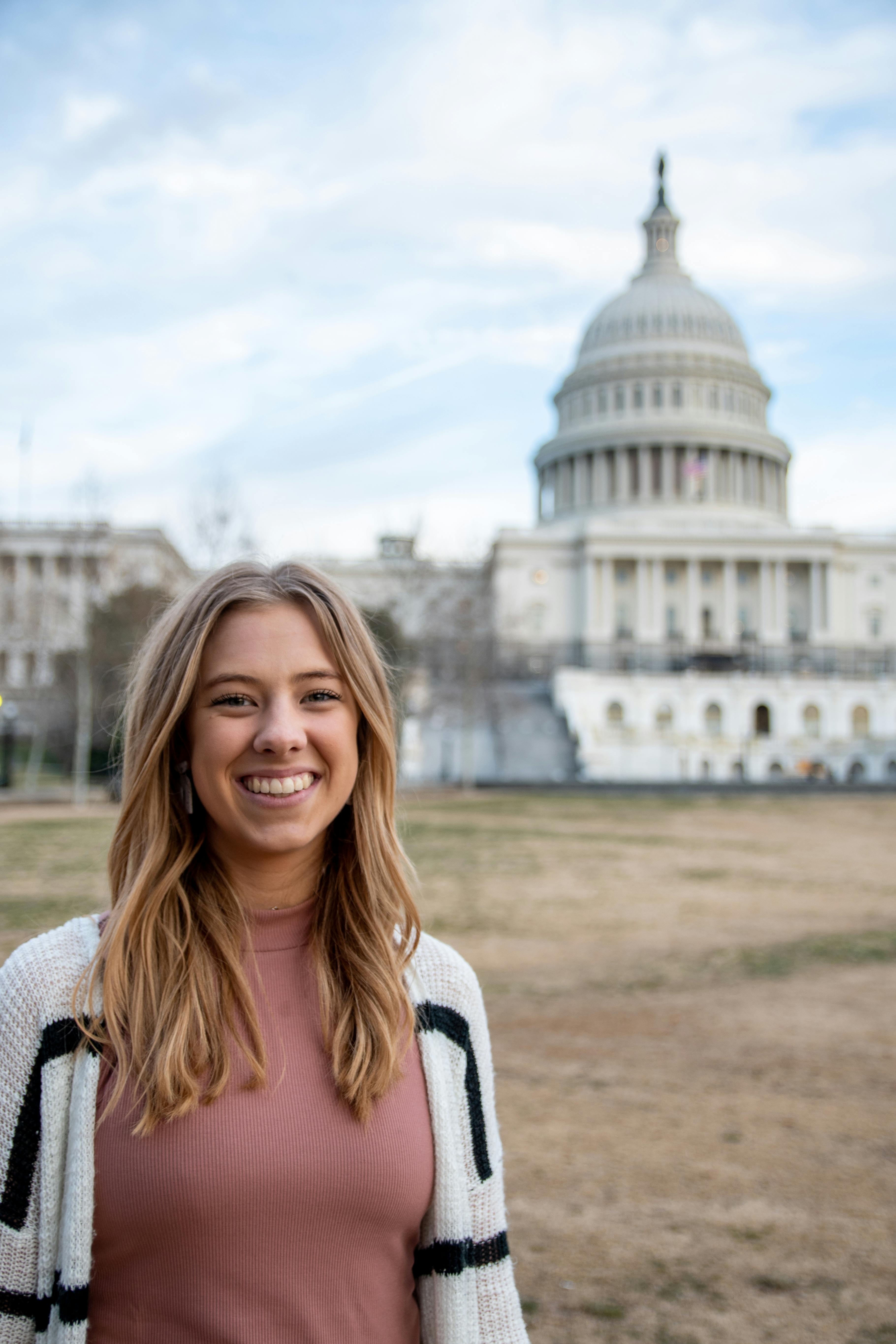 A cheerful young woman posing with the iconic US Capitol Building in the background.