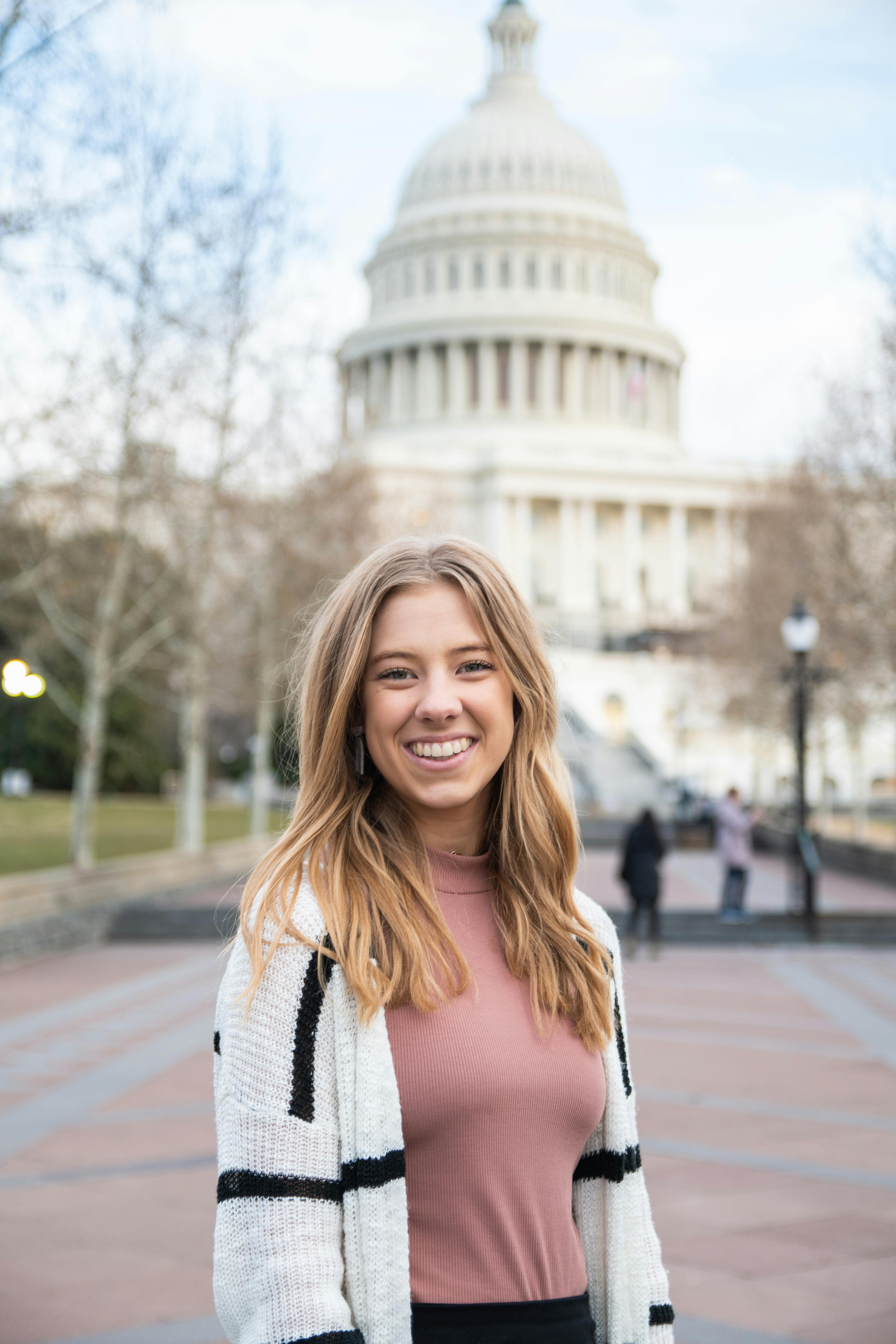 Smiling woman in casual attire stands confidently with the iconic US Capitol in the background.