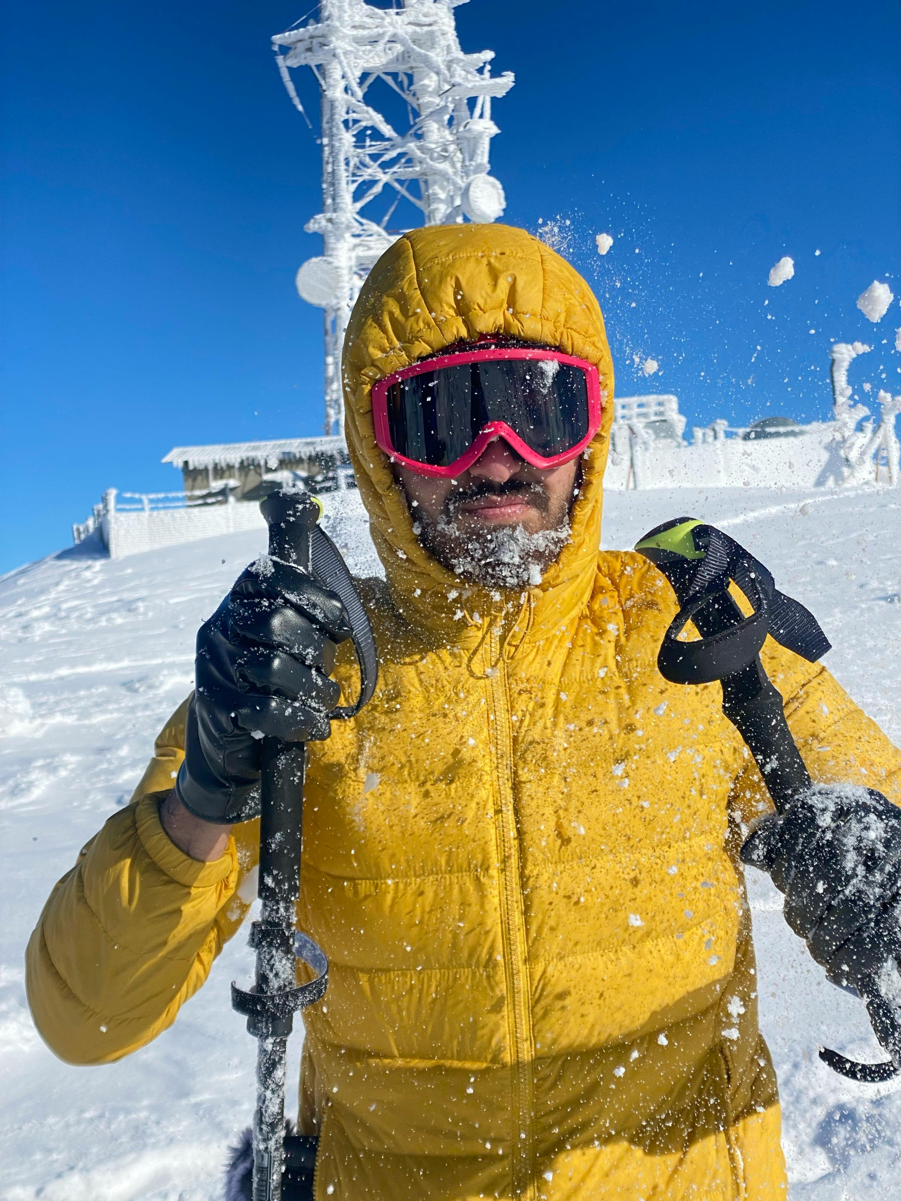 Prescription Goggle Inserts - A man in a yellow jacket hiking through snow in Iraq, using trekking poles under a bright blue sky.