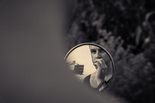 Grayscale Photo of a Man's Reflection in the Round Mirror