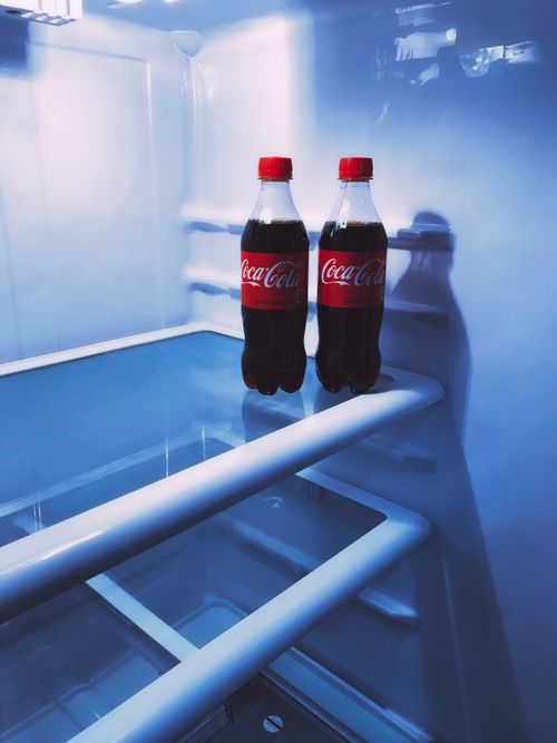 Free Two Coca-Cola bottles inside a refrigerator, showcasing the cool refreshing drink. Stock Photo