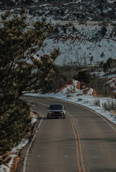 A vintage car drives along a winding road in a snowy mountain landscape, capturing a sense of adventure.