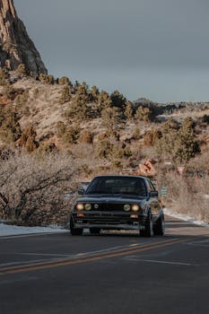 Vintage black car cruising on a scenic mountain road during daytime.
