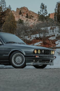 Vintage BMW E30 sedan in a snowy mountain landscape, showcasing its iconic design and elegance.