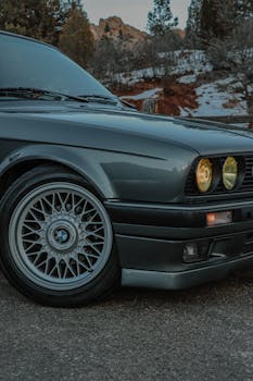 Classic BMW E30 with stylish rim against a scenic outdoor backdrop offering automotive elegance.