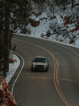 A black car drives on a winding road surrounded by snow-covered scenery.