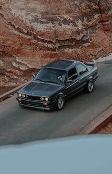 A sleek BMW E30 parked on a mountain road, surrounded by red rocky terrain under a cloudy sky.