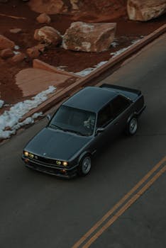 Classic car driving on a scenic road surrounded by snow and rocks. High angle shot.