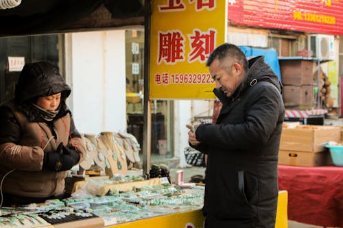 A Man and Woman in Brown and Black Jacket Standing Near the Stall