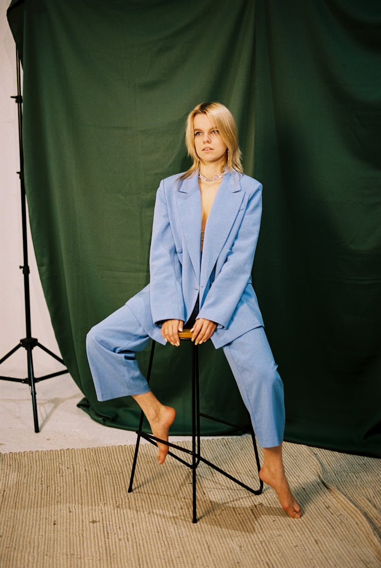  Blond Woman Wearing Blue Suit Sitting On Bar Stool