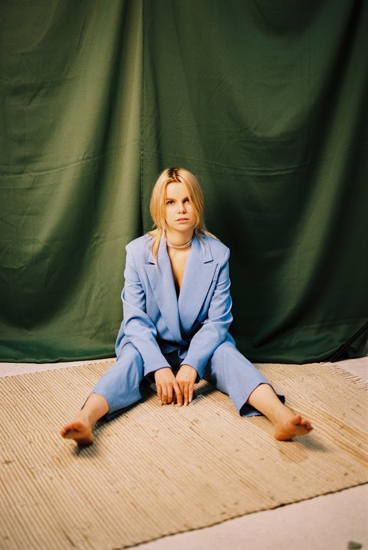 Young Blond Woman Sitting On Straw Mat In Blue Suit