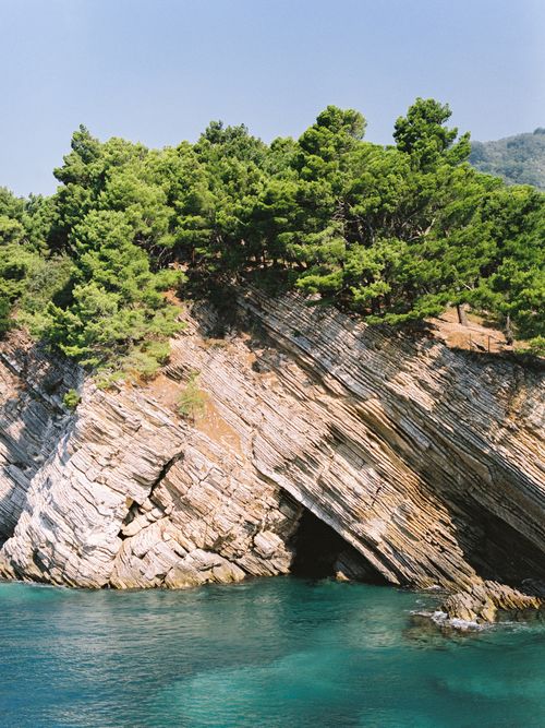 Free Beautiful coastal scene featuring rock formations and pine trees by a turquoise sea under clear blue skies. Stock Photo