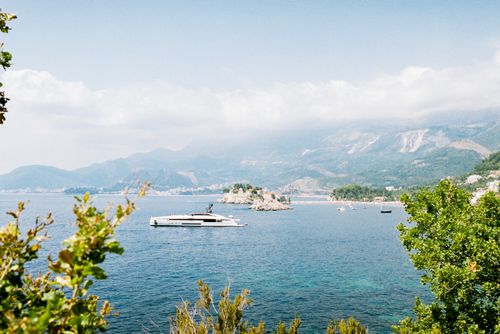 Free A beautiful coastal view featuring a yacht sailing near lush green hills and a distant city. Stock Photo