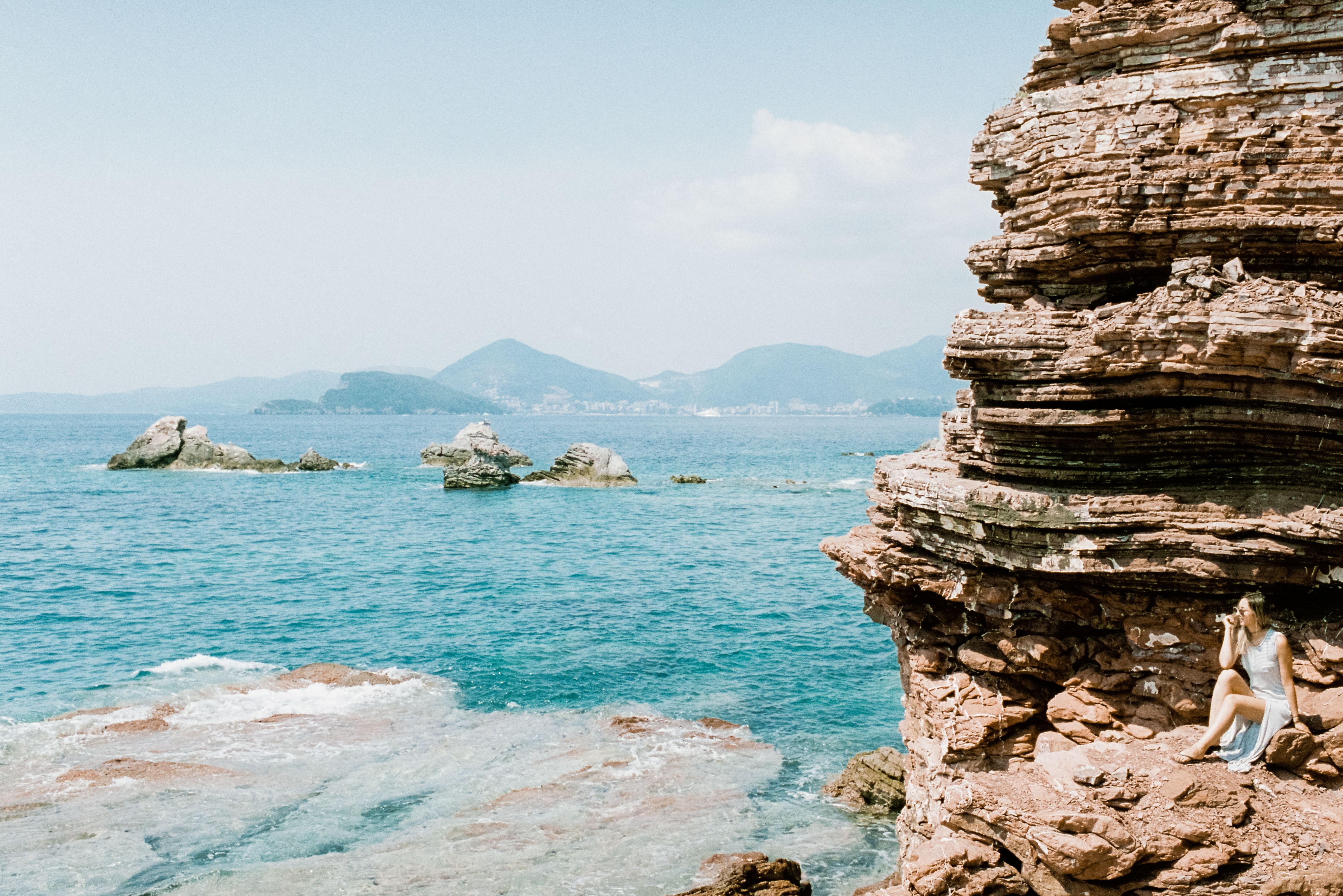 Woman Sitting near Rocks on Sea Shore · Free Stock Photo