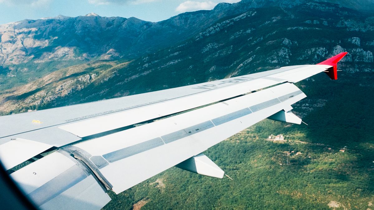 View from airplane window showing wing and scenic mountains below, capturing aerial travel experience.
