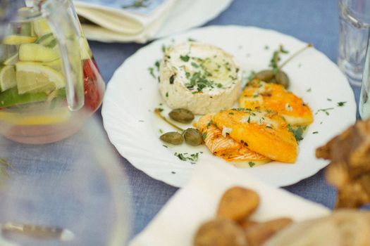 Elegant gourmet cheese plate with citrus, herbs, and a refreshing drink on a dining table.