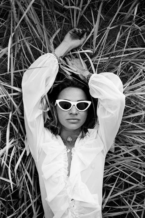 Free Grayscale of a Woman Wearing Sunglasses Lying on Grass Stock Photo