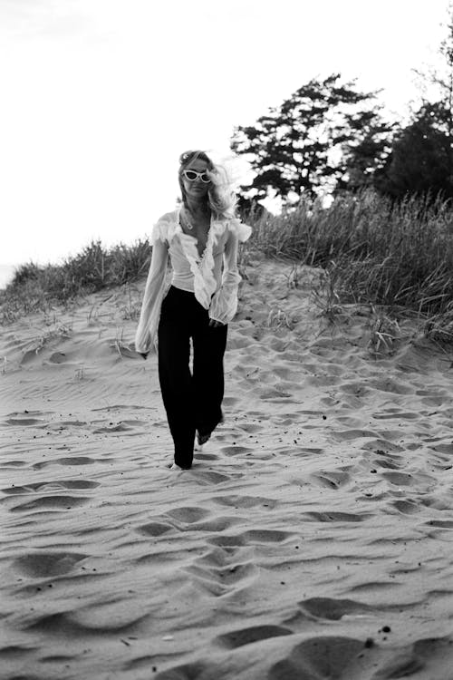 A Woman in White Long Sleeves and Black Pants Walking on the Sand