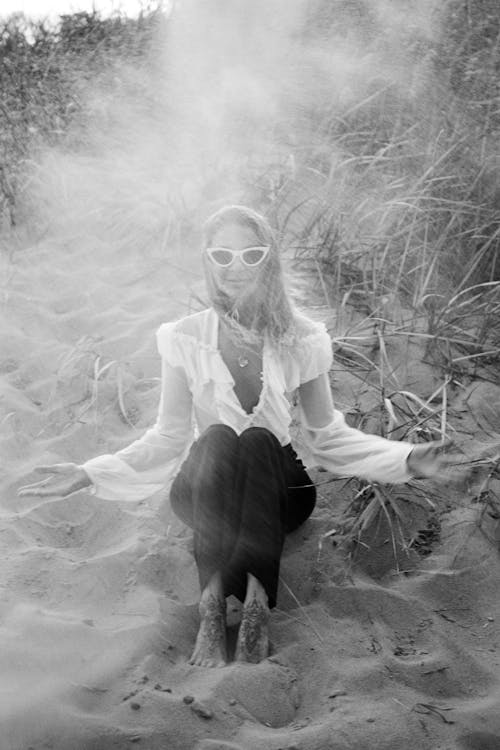 A Woman in White Long Sleeves and Black Pants Sitting on the Sand