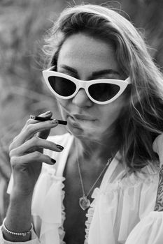 Chic black and white portrait of a woman wearing sunglasses and smoking.