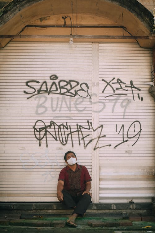 A Man Wearing Face Mask Sitting in Front of a Roll Up Door