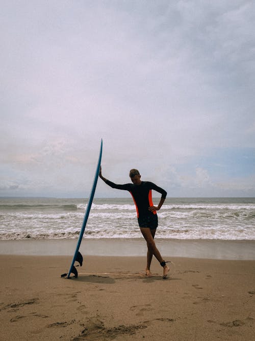 A Man in Black Rash Guard Standing Near the Surfboard