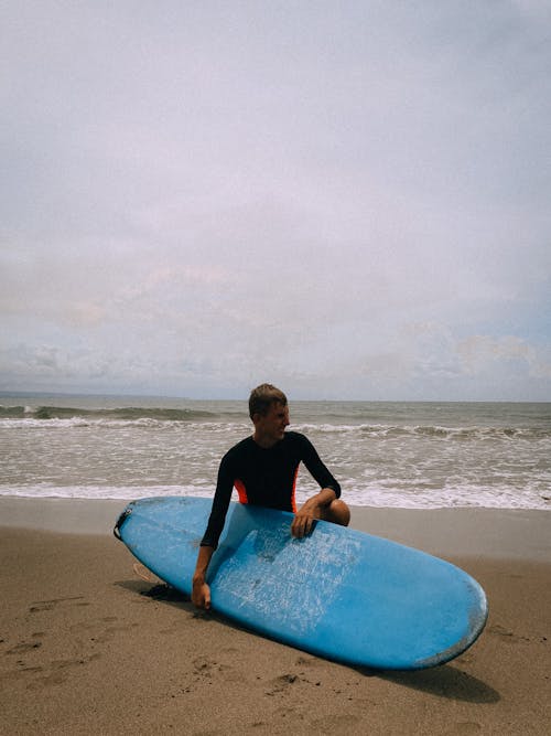 Photo of a Man Holding His Blue Surfboard on the Sand