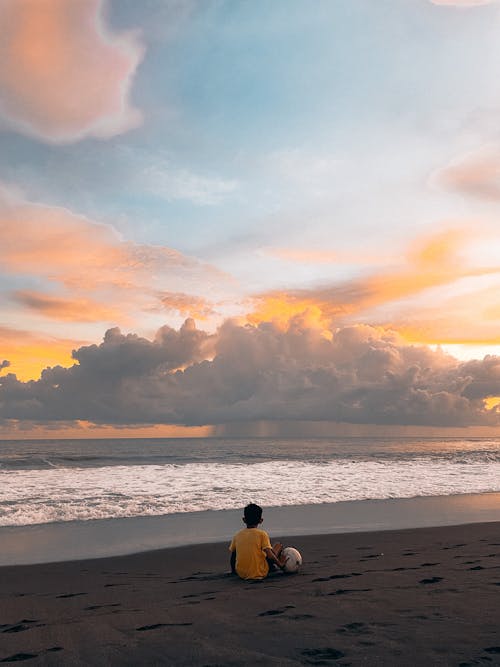 A Person in Yellow Shirt Sitting on the Beach Sand