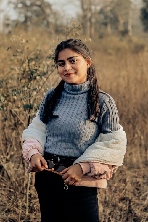 Free A young woman in a stylish outfit smiles outdoors in a natural autumn setting. Stock Photo