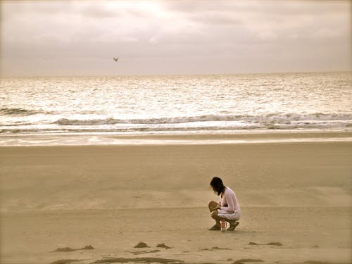 Free Woman in Pink Cardigan Sitting on Seashore Stock Photo