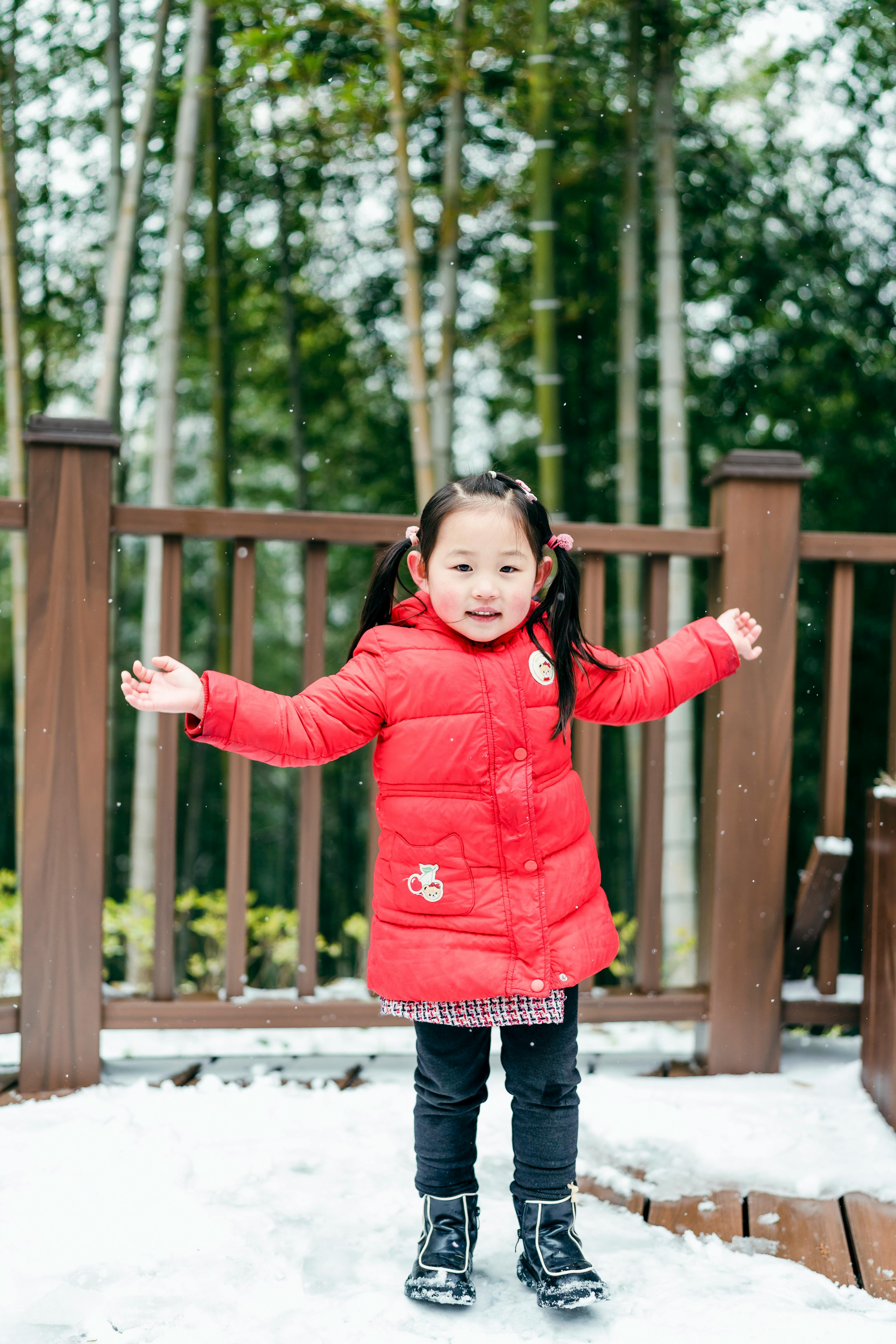 Young girl in bright red jacket having fun in the winter snow outdoors.