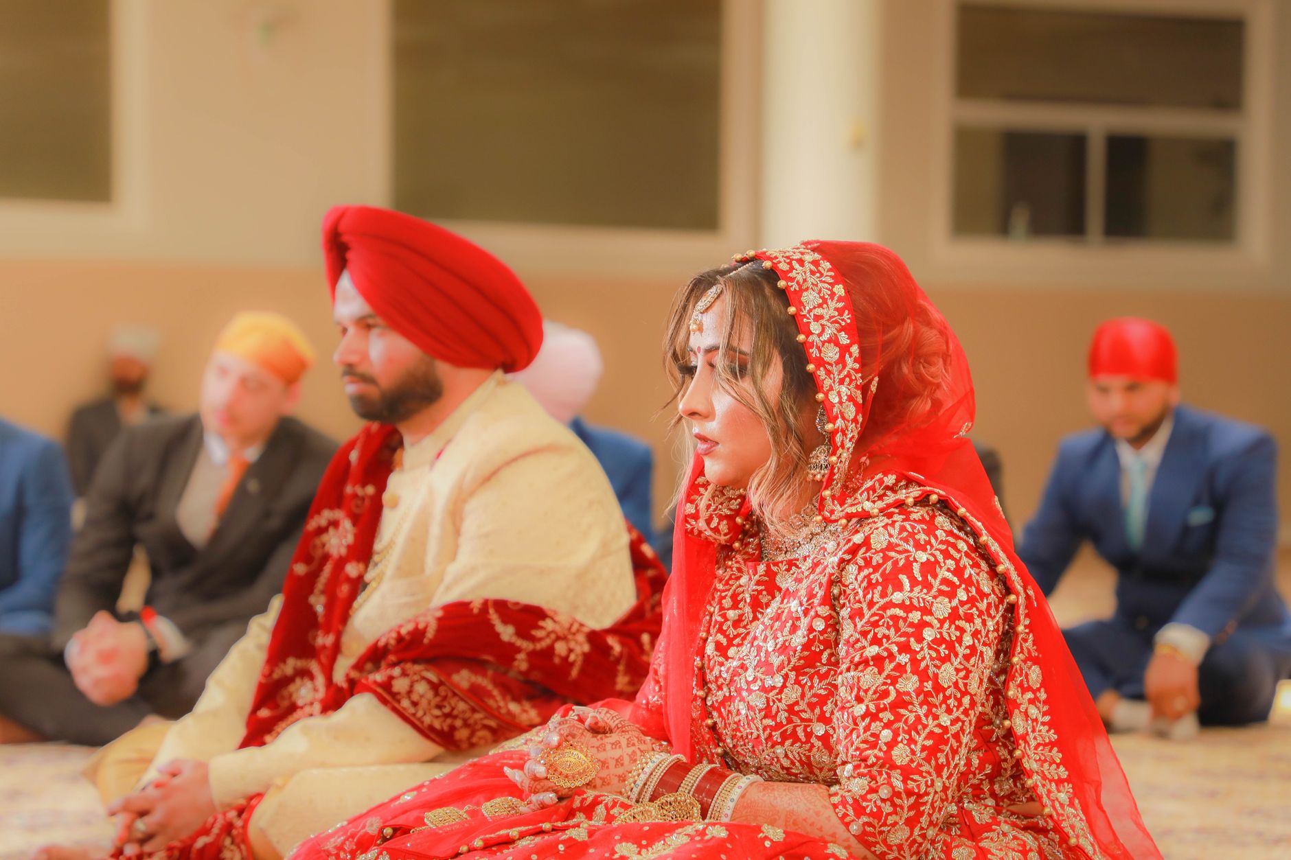 A bride and groom in traditional attire during an Indian wedding ceremony inside a venue.