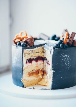 Close-up of a layered cake with chocolate, pretzels, and berries, elegantly decorated.