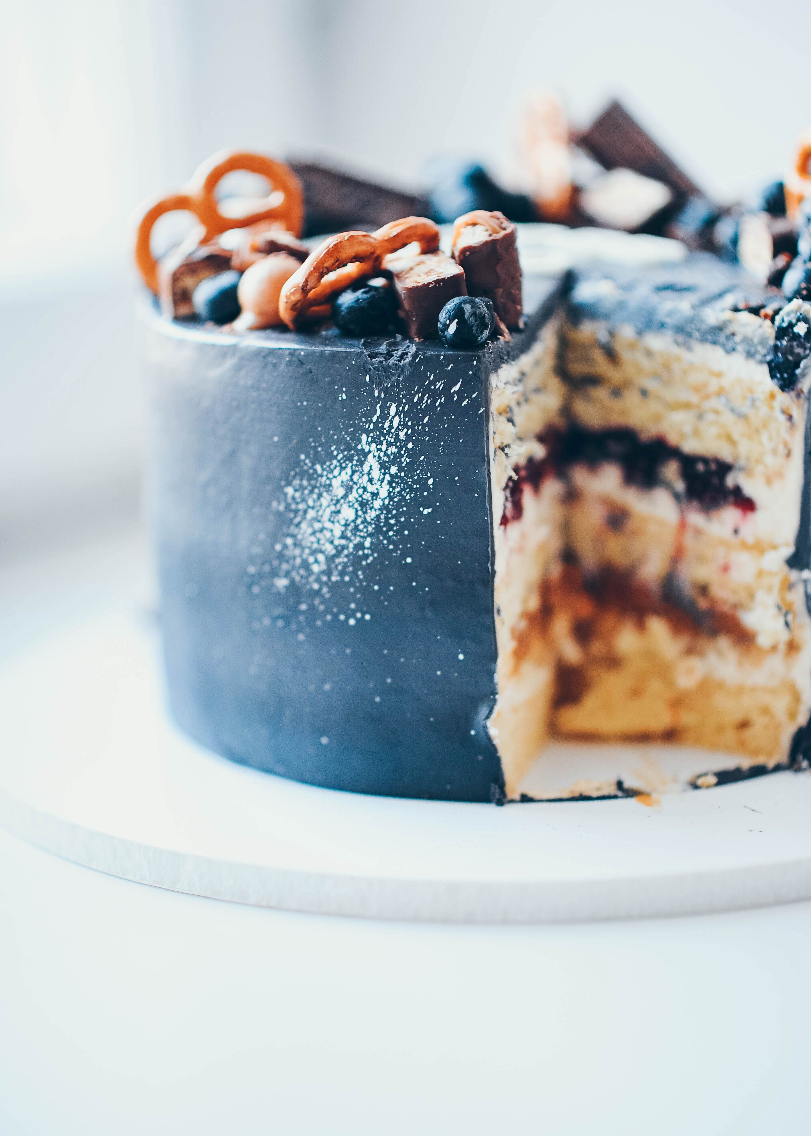 Sliced chocolate cake with blueberries, pretzels, and chocolate bars in a close-up view.