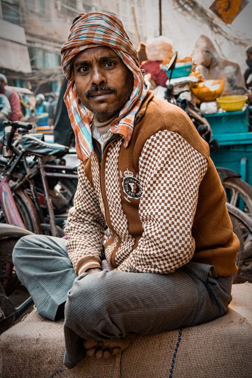 Free A man wearing a checkered jacket and turban sits on a bustling street. Stock Photo