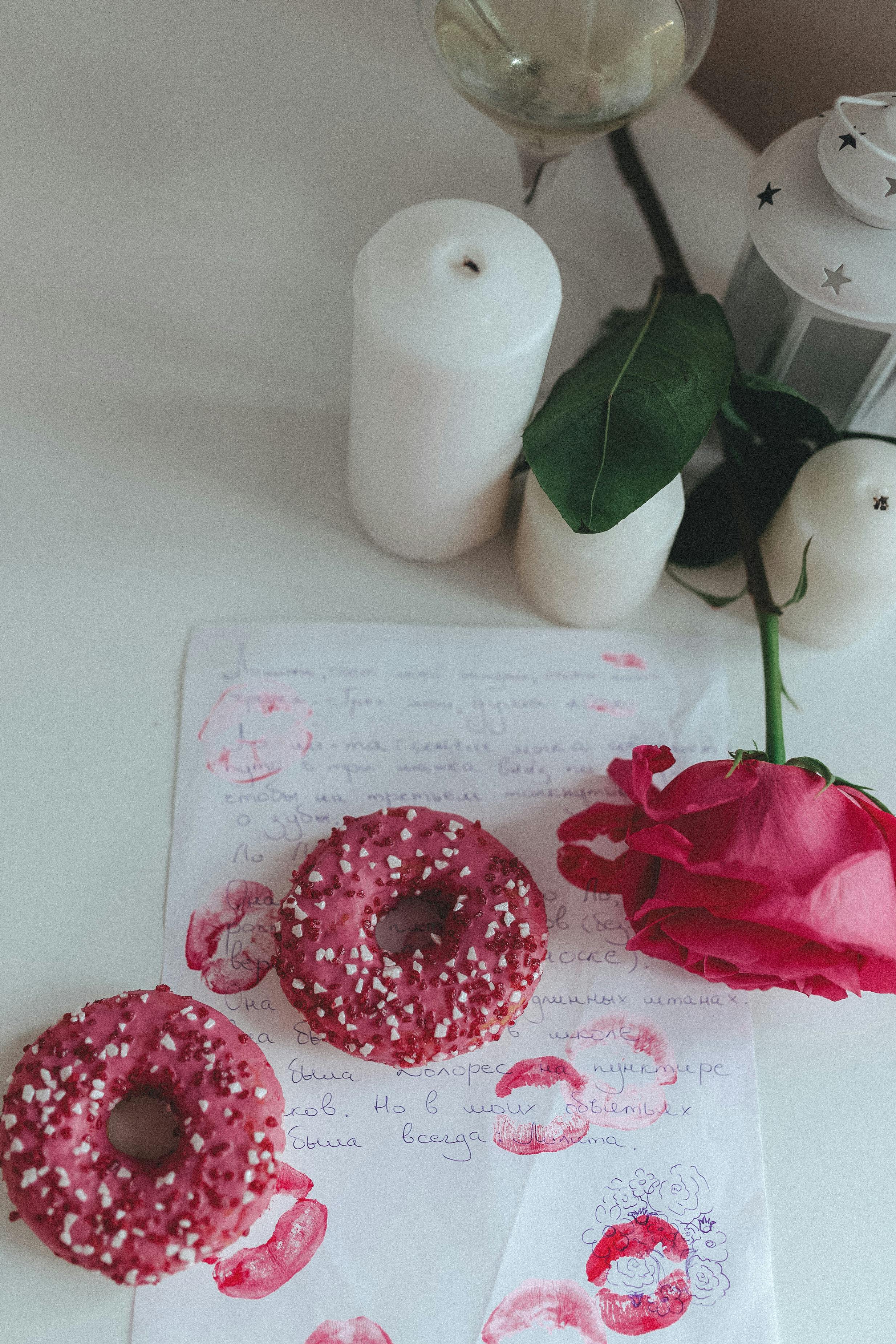 A romantic flat lay scene featuring donuts, a rose, candles, and a love letter with kiss marks.
