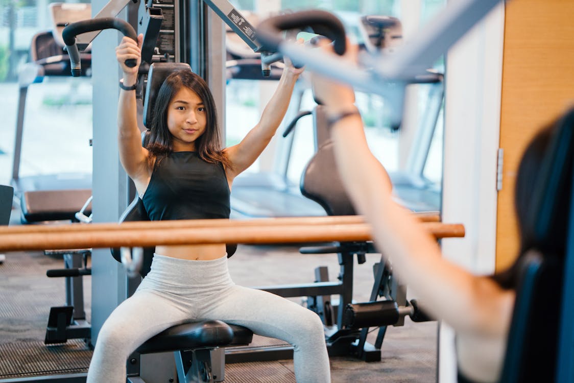 Woman in Black Sleeveless Crop-top and White Leggings Using a Butterfly Machine in Front of a Mirror