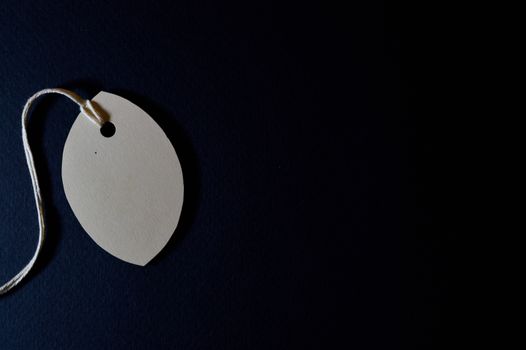 Close-up of a blank paper tag with string on a dark background, perfect for customizable designs.