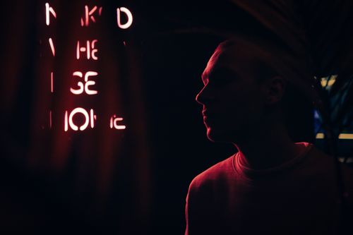 Free A man's silhouette illuminated by a neon sign in a moody, dark environment. Stock Photo