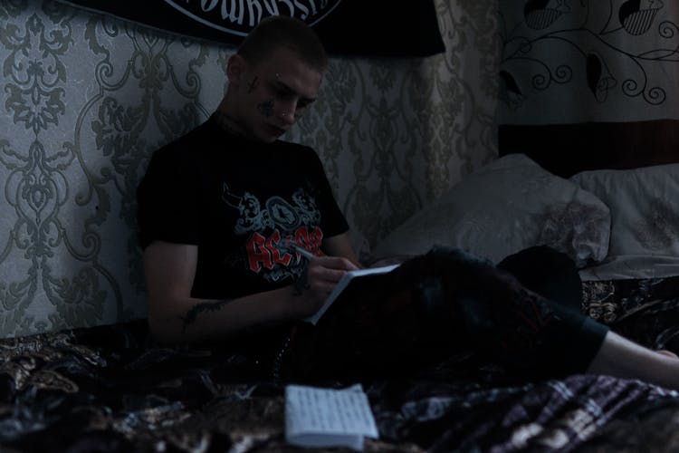 A Tattooed Man Writing In Bed