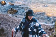 Man in Black and White Plaid Dress Shirt Wearing Black Cap Holding Walking Stick Near Body