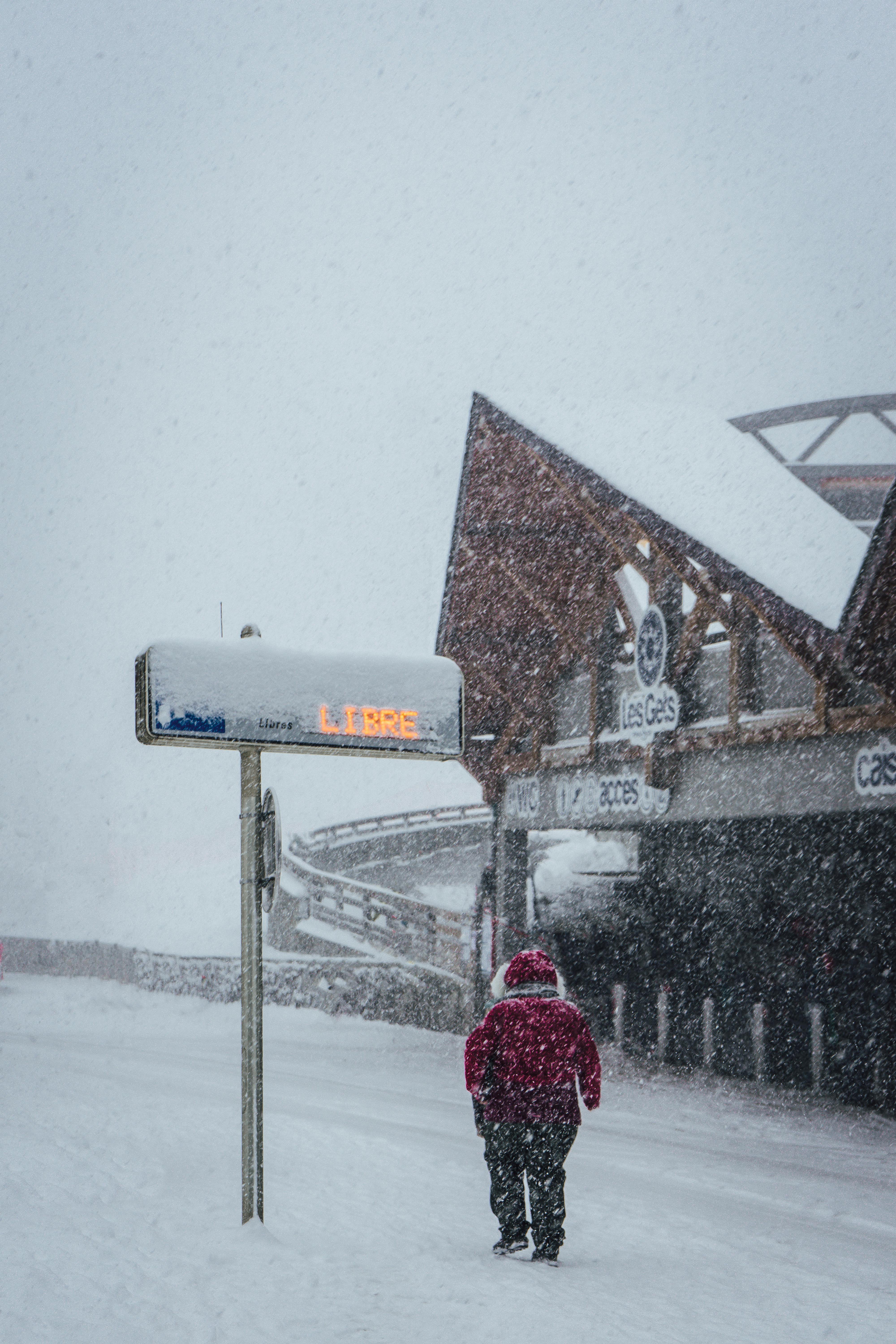 A person walks through heavy snowfall at Les Gets, France, wearing a red jacket.