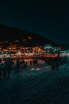 Illuminated buildings and crowds in snowy Les Gets at night.