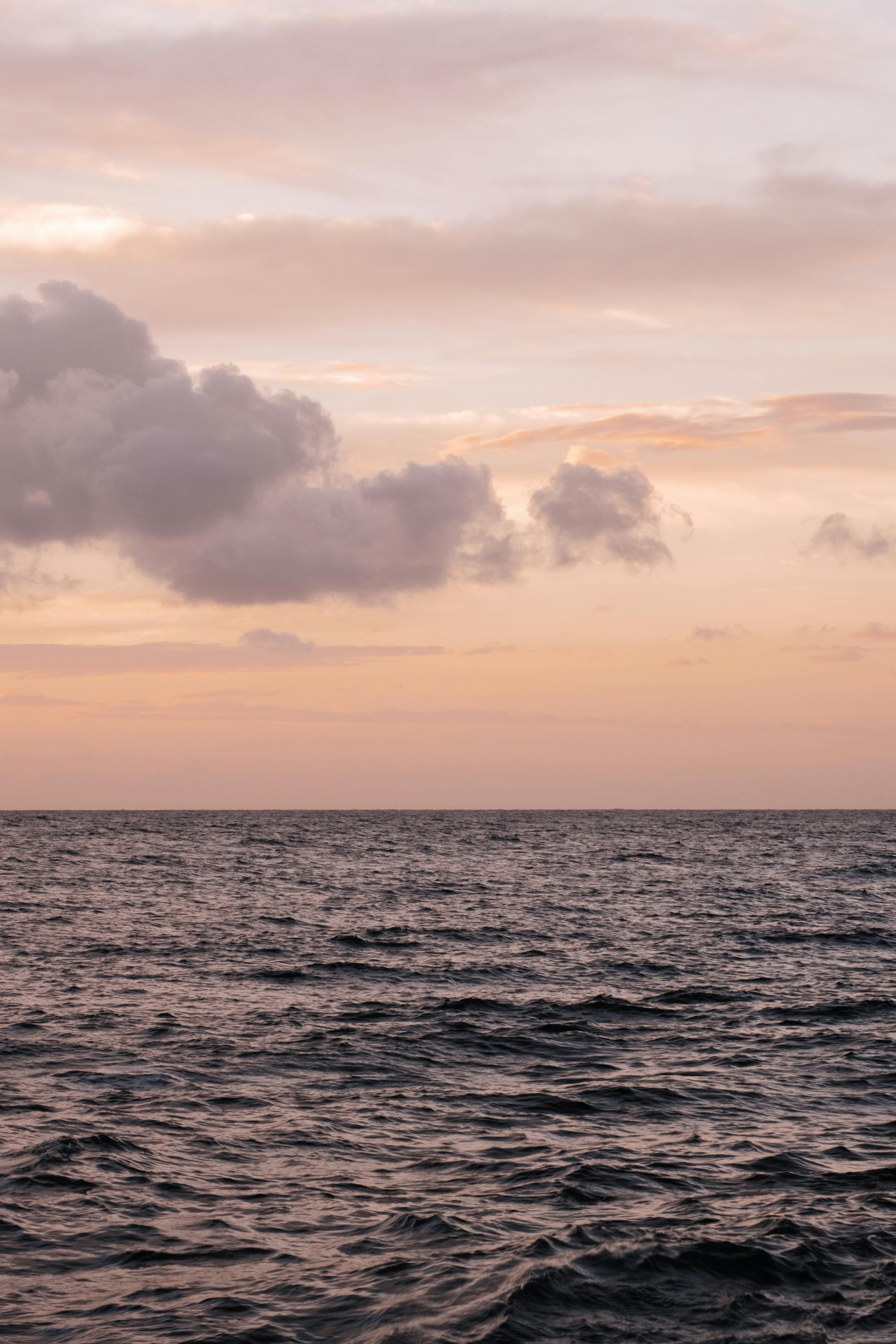 Calm ocean waves under a beautiful sunset sky with clouds on the horizon.
