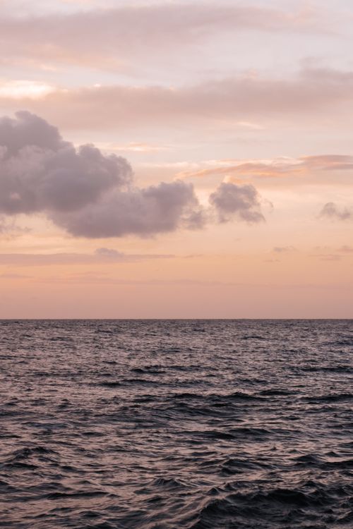Free Calm ocean waves under a beautiful sunset sky with clouds on the horizon. Stock Photo
