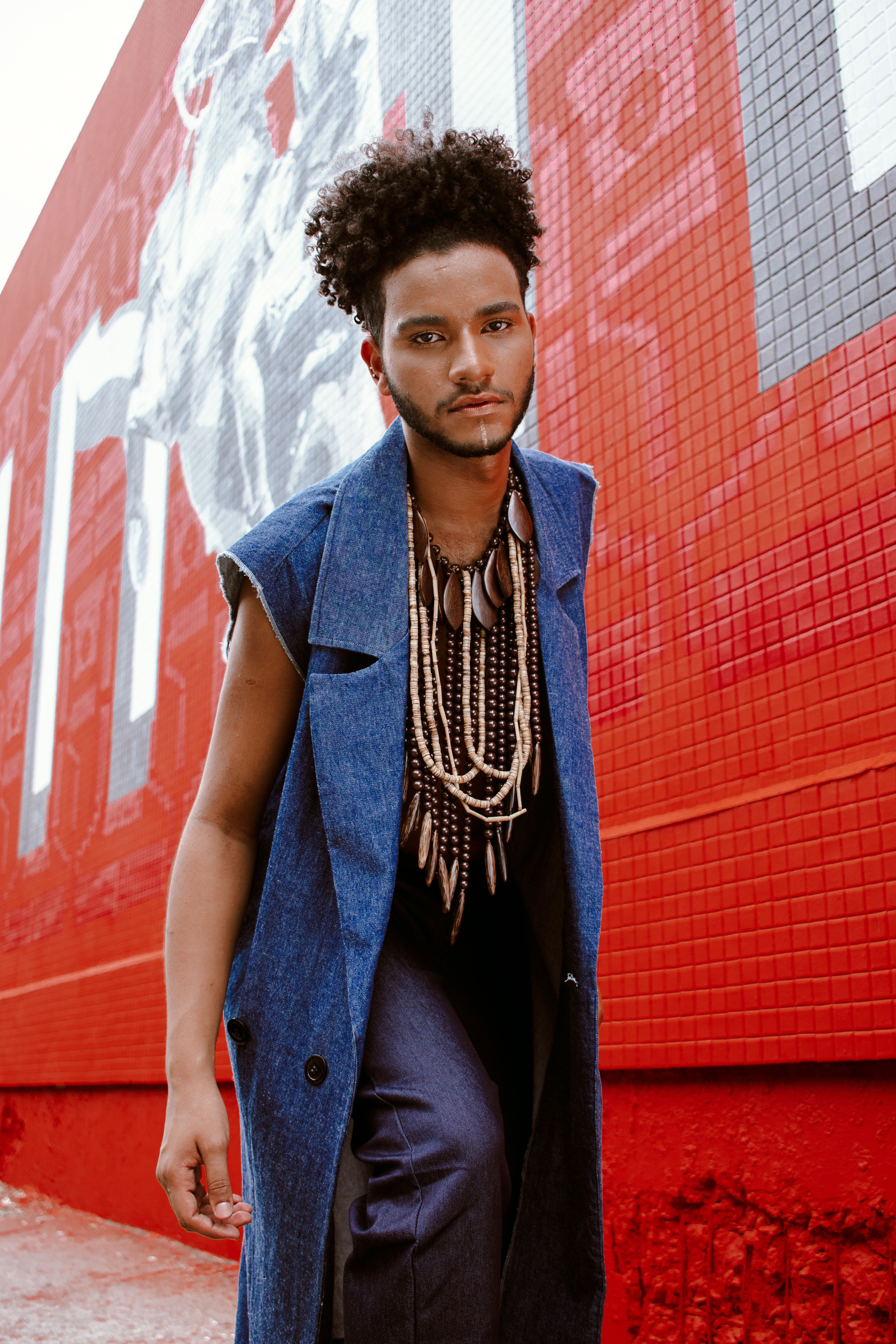 Stylish young man with curly hair poses in front of a vibrant mural in Belo Horizonte, Brazil.