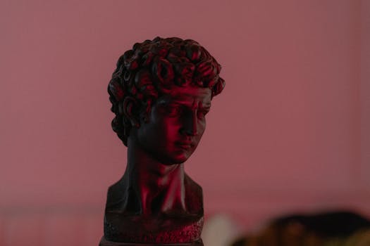Atmospheric image of a classical David bust illuminated by moody red light in a blurred background.