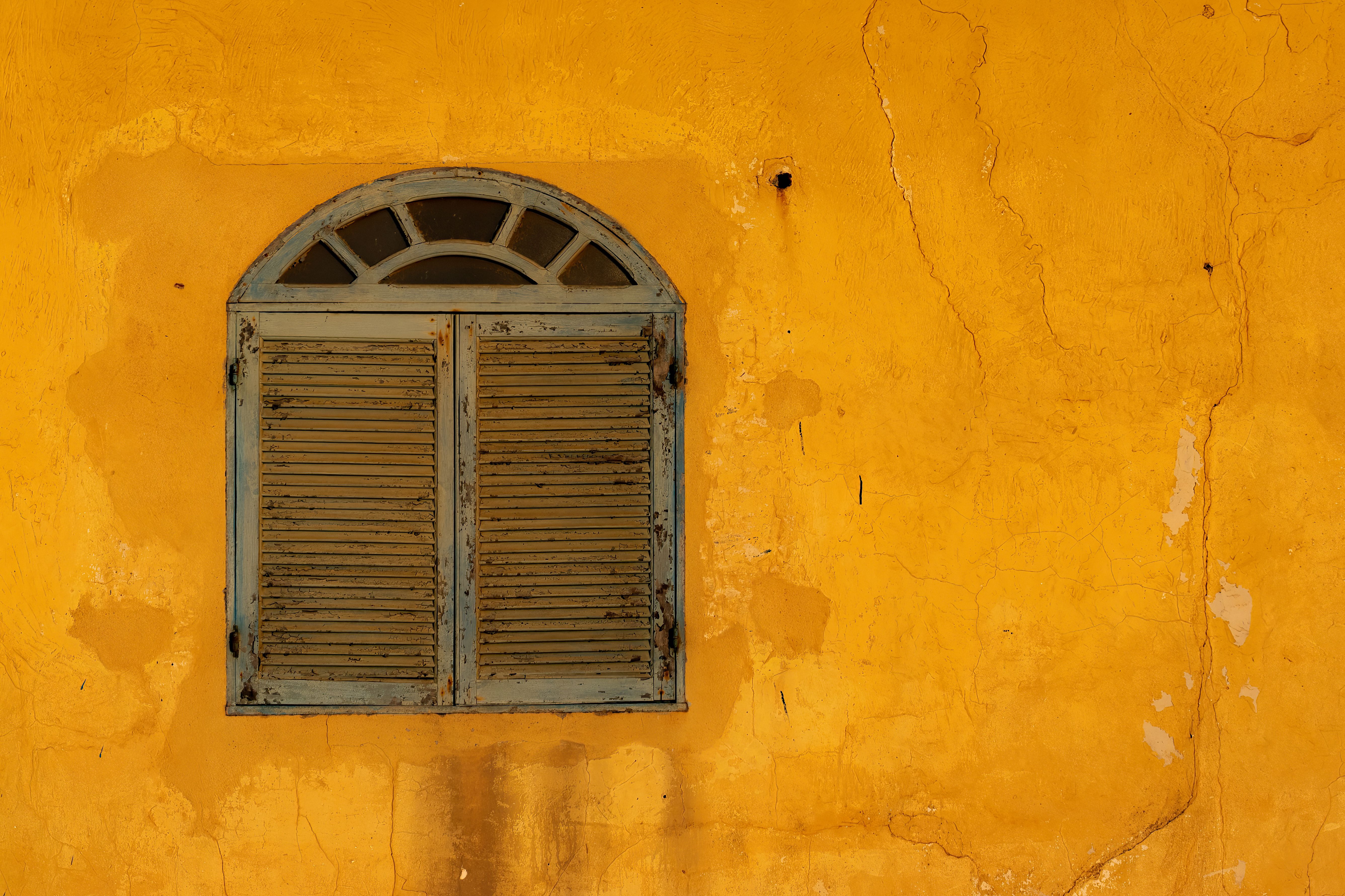 A rustic yellow wall featuring a weathered, shuttered vintage window, creating an old-world charm.