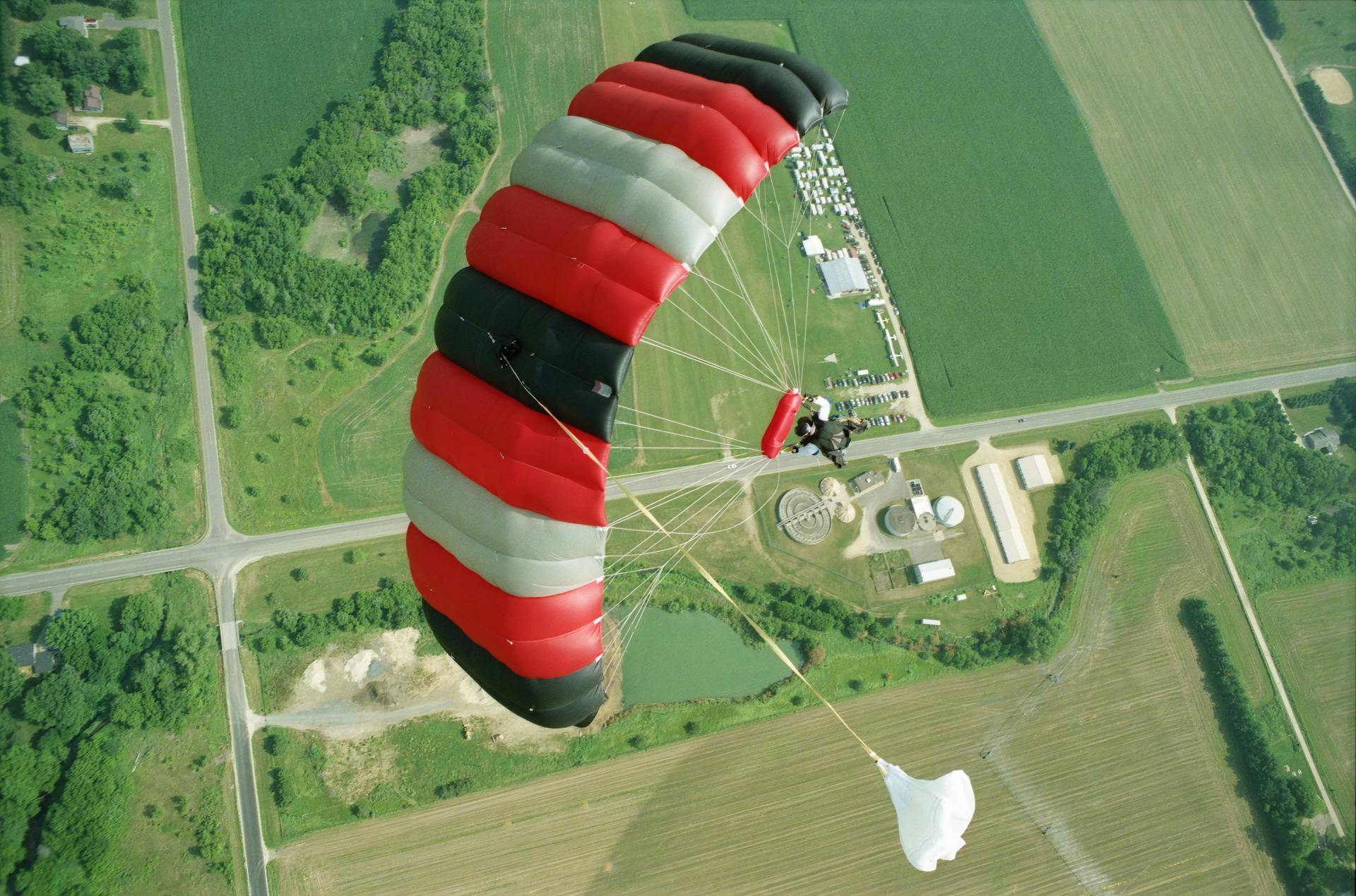 Aerial view of a skydiver gliding over Baldwin, WI fields with a colorful parachute.