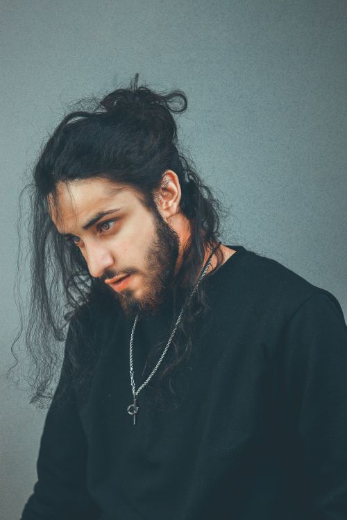 Free Stylized portrait of a man with long hair and beard wearing a black sweater and necklace. Stock Photo